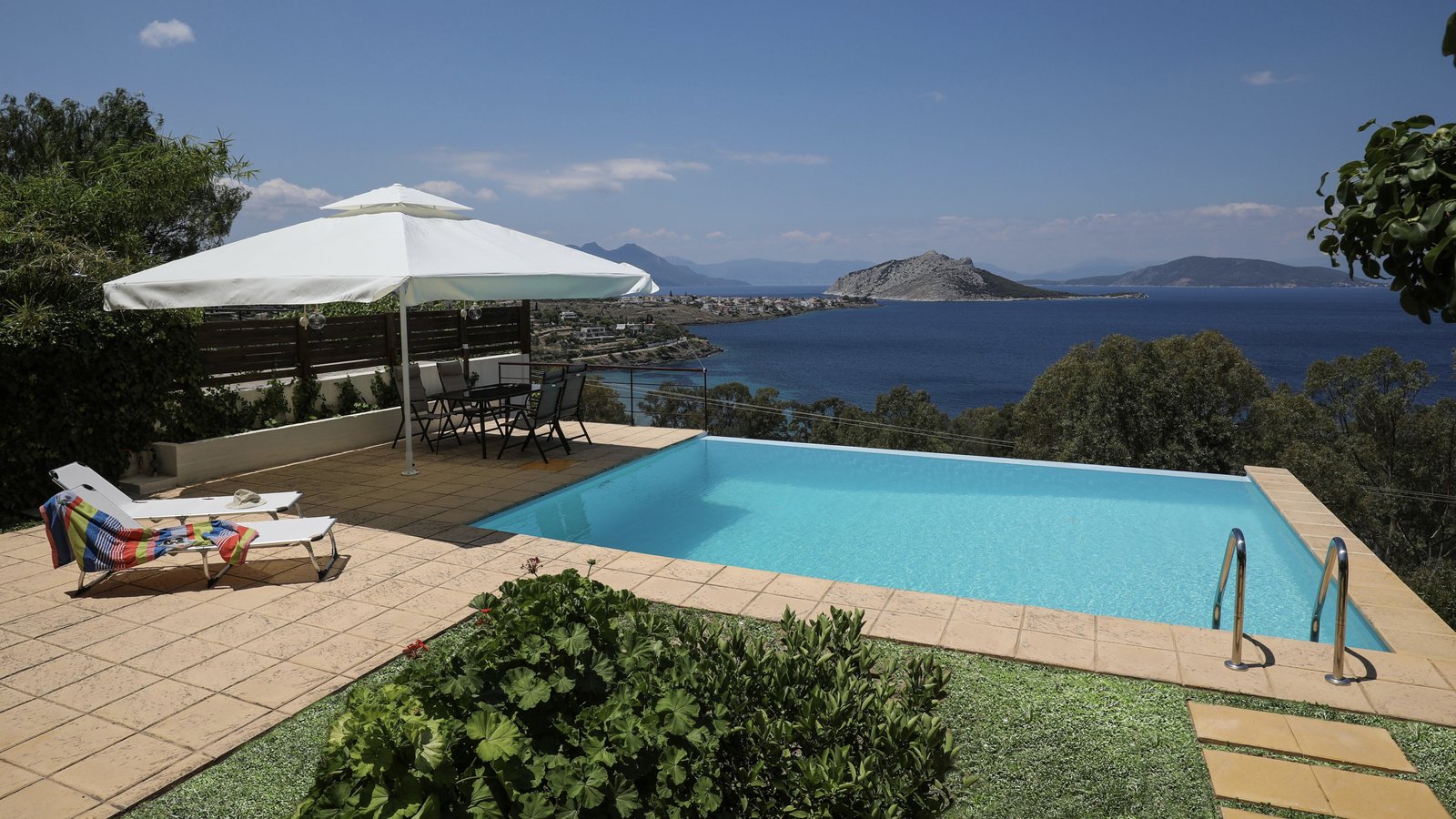 Panoramic view from a terrace with an infinity swimming pool and sunbeds under an umbrella