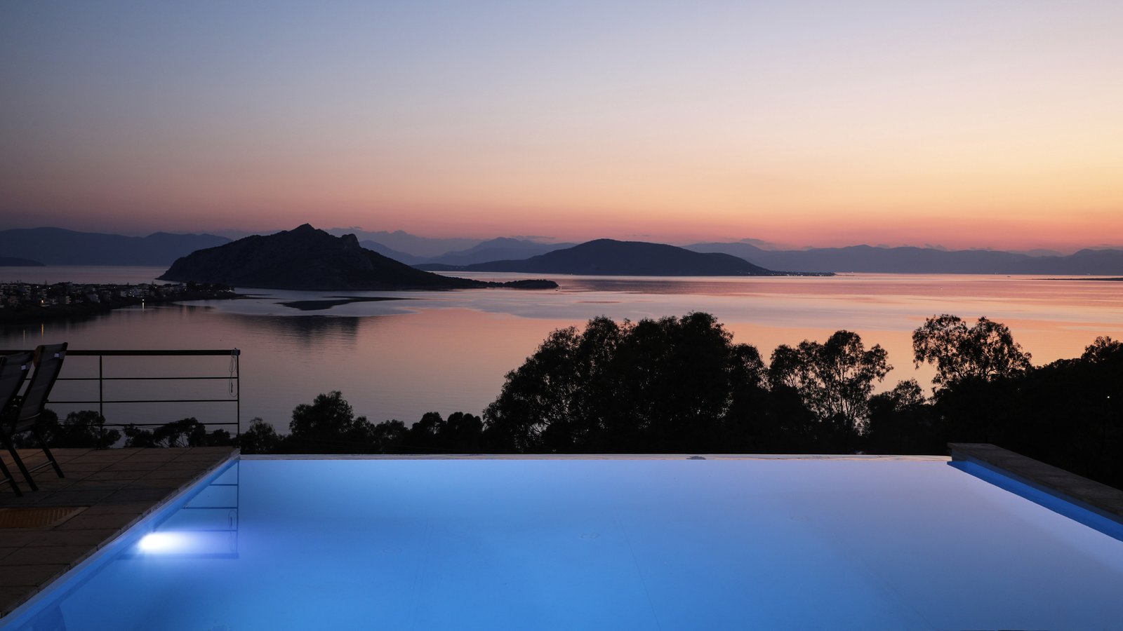 Panoramic night view to the islands of Moni and Agistri in front of an infinity swimming pool