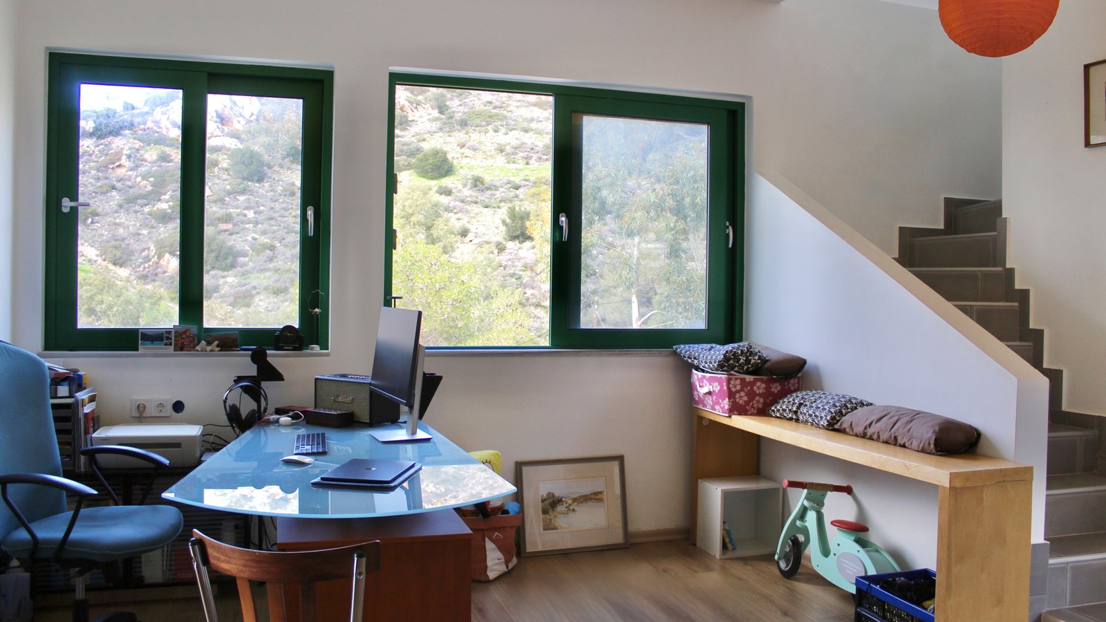 Overview of the office area/secondary living room and the staircase leading to the fourth level of Eucalyptus Duplex in Aegina, Greece. There area also big windows with a view to the mountain